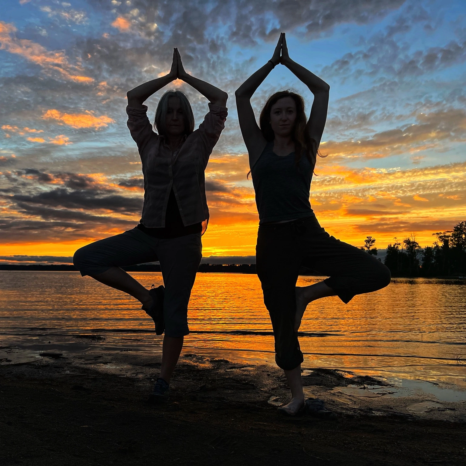 yoga PMEZ founders striking a tree pose on the shore of Lake Champlain